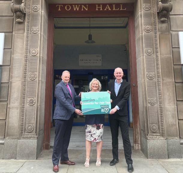 Preston City Council Chief Executive Adrian Phillips, Cllr Anna Hindle and Leader of Preston City Council outside Preston’s Town Hall Preston City Council's Chief Executive, Councillor and Leader hold the Councils for Fair Tax banner